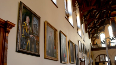 A wall with several paintings of people hanging on it.