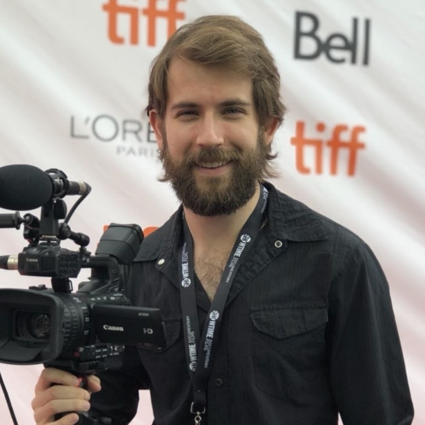 A man holding a camera and smiling for the camera.