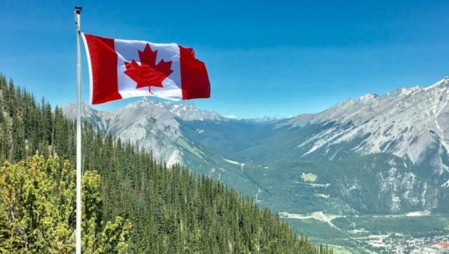 A canadian flag flying over the mountains.