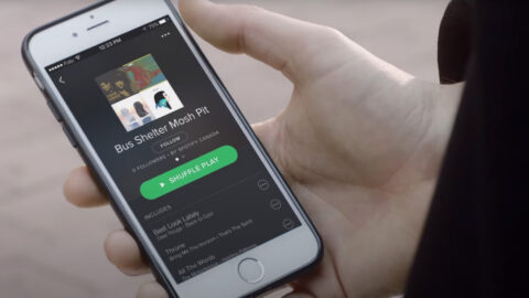 A person holding an iphone with the spotify app open.
