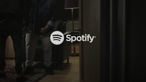 A person standing in front of a wall with the logo for spotify.