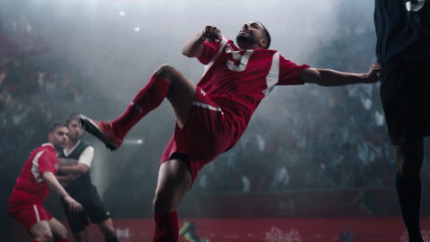 A man in red shirt kicking a soccer ball.