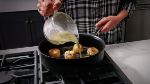 A person pouring oil into a pan of food.