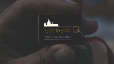 A close-up of a hand holding a black keychain with the logo "empirent prague luxury suites" against a blurred background.
