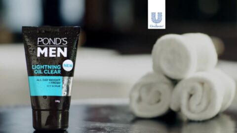 A tube of pond's men lightning oil clear face scrub on a counter, with neatly rolled white towels in the background.