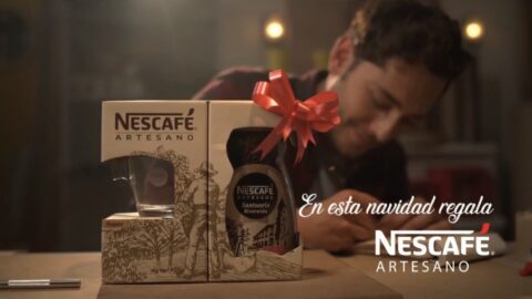 A man views a nescafé artesano coffee gift set on a table, adorned with a red bow, under warm lighting, with promotional text suggesting it as a christmas gift.
