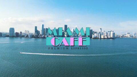 Aerial view of miami's skyline with "miami café premium espresso" logo superimposed over the image, featuring stylized mountains and a speedboat in the water.