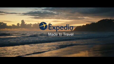 Sunset on a beach with waves in the foreground and trees lining the shore, featuring the expedia logo and the slogan "made to travel.