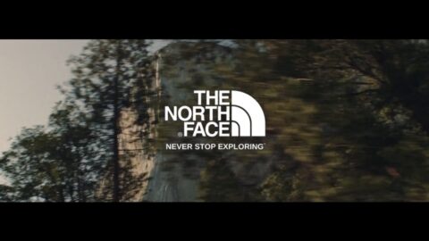 The north face logo with the slogan "never stop exploring" displayed over a blurred natural landscape.