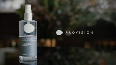 A bottle of "provision dream extract" spray on a blurred greenery background, providing a serene and elegant presentation.
