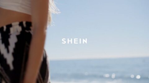 A close-up shot of a person wearing a black and white garment with the word "shein" overlaid, against a blurred beach background.